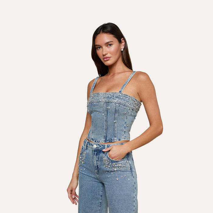 Wearing the Arlin Embellished Tank and cropped jeans adorned with pearls and rhinestones, a woman stands with one hand in her pocket against a plain background.