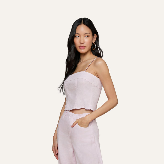 A woman with long dark hair wears the Arlin Linen Tank in light pink with matching pants, standing with one hand in her pocket against a plain, off-white background.