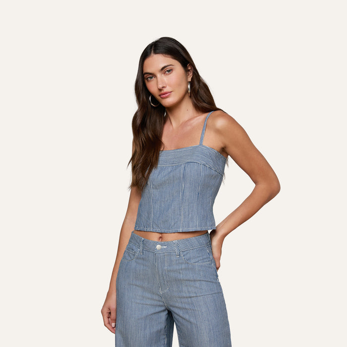 A woman with long brown hair is wearing the Arlin Tank—a blue striped sleeveless top—paired with matching pants, standing with one hand on her hip against a plain light background.