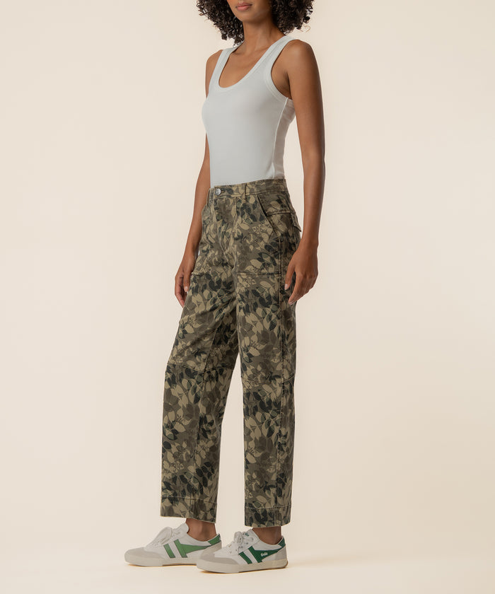 Woman wearing white sleeveless tank top and olive camouflage relaxed-leg pants with white and green sneakers.