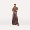 A woman stands against an off-white background, wearing a cardamom brown short-sleeve knit top paired with the Aubrie Satin Pant—a high-waisted, wide-leg trouser in a matching shade—styled with large earrings and open-toe shoes.
