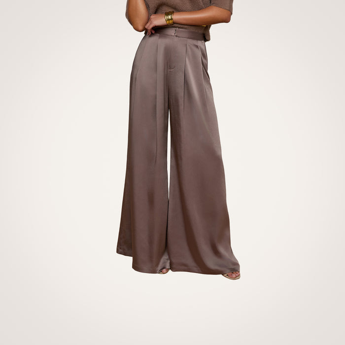 A person wearing the Aubrie Satin Pant in cardamon brown, paired with a coordinating brown top and gold bracelets on their wrist, stands against a light background.