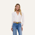 A woman with long blonde hair wears the Ava Blouse, a vintage-inspired ivory top featuring scalloped guipure lace cuffs, paired with blue jeans. She stands facing forward against a plain light background.