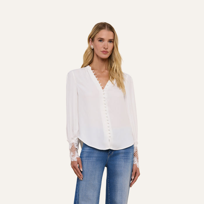 A woman wearing the Ava Blouse—an ivory, vintage-inspired top with scalloped guipure lace cuffs—and blue jeans stands against a plain light background, facing forward with a neutral expression.
