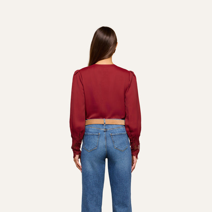 A woman with long brown hair, seen from behind, wears the Ava Blouse—featuring vintage-inspired scalloped lace detailing—paired with blue jeans, standing against a plain light background.