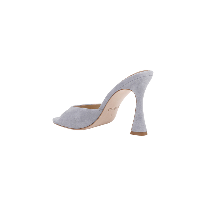 The Avery Suede Open-Toe Mule is a light gray heeled mule shoe with an open back and peep toe, featuring a flared sculpted high heel and soft suede texture. Displayed on a plain white background, it is enhanced with a memory foam insole for added comfort.