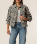 Tan and brown leopard print denim jacket with collar, button front, and chest pockets worn over white top.
