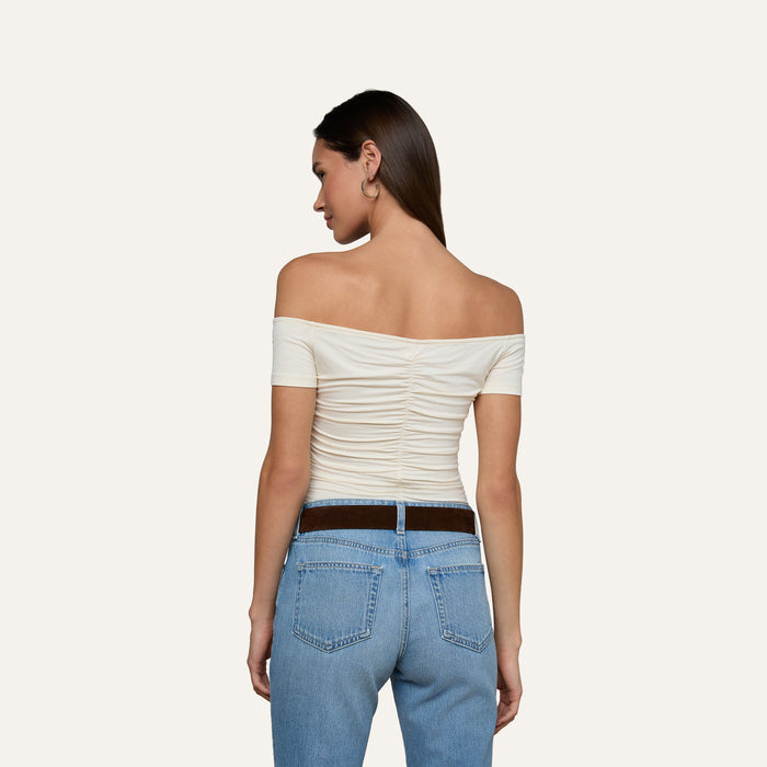 A woman is standing with her back to the camera, wearing the vintage-inspired white Baliegh Ruched Bodysuit and light blue jeans.