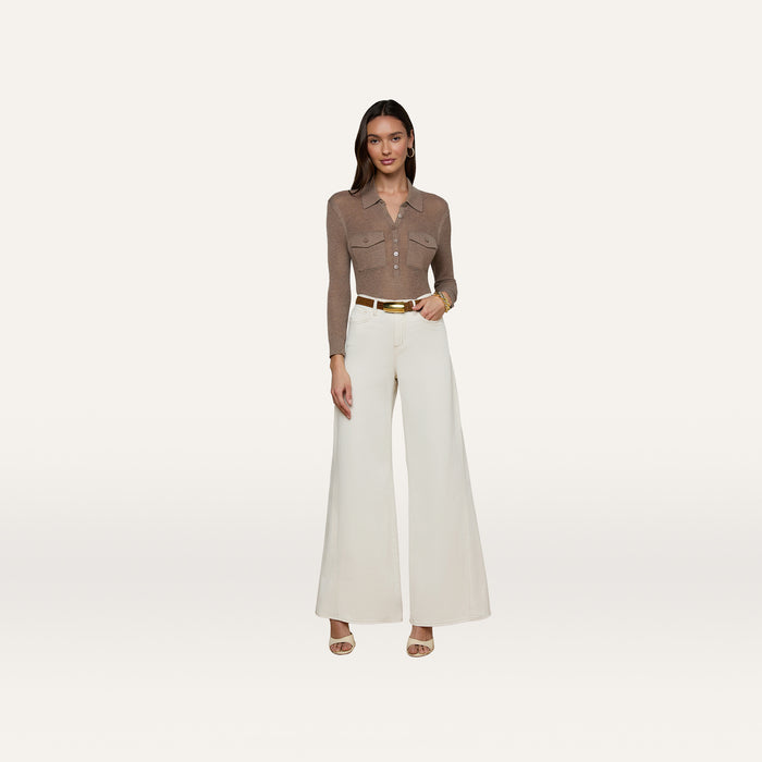 A woman stands against a plain white background wearing a brown collared long-sleeve shirt, the Beau Wide-Leg Jean in high-rise stretch cotton twill in white, a white belt with a gold buckle, and beige heels.