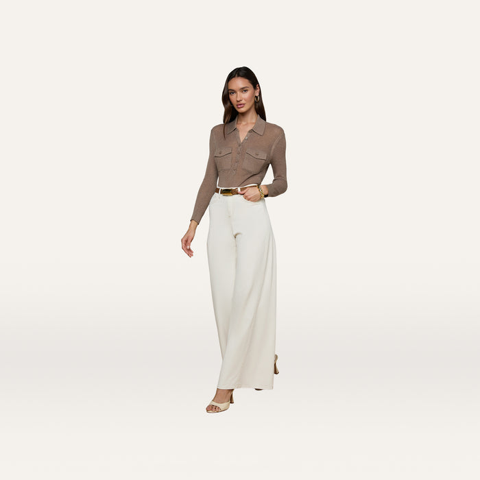 A woman walks confidently against a plain white background, wearing a brown long-sleeve blouse tucked into the Beau Wide-Leg Jean—a high-rise, wide-leg style in stretch cotton twill—paired with a tan belt and beige heels.