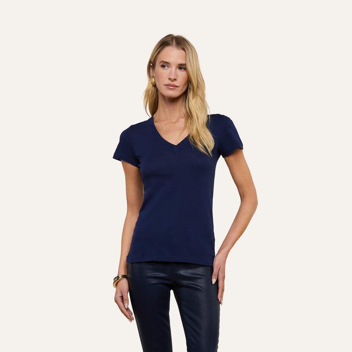 A person with long blond hair is wearing the Becca Cotton V-Neck Tee in navy and black pants, standing against an off-white background.