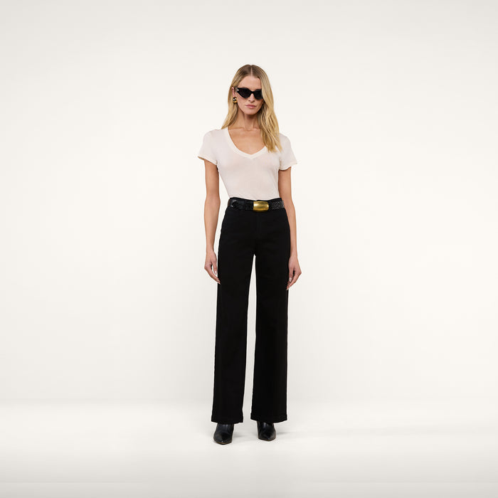 A woman stands against a plain background wearing sunglasses, black wide-leg belted pants, black shoes, and the Becca Cotton V-Neck Tee—a vintage-inspired off-white 100 cotton top.