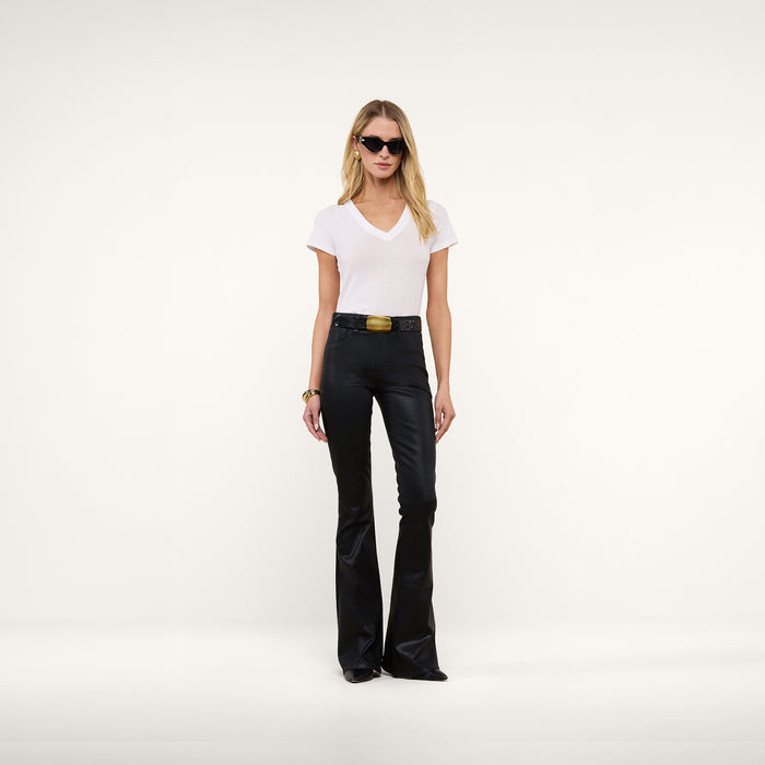 A woman wearing sunglasses, the Becca Cotton V-Neck Tee in white, black belted flared pants, and black shoes stands against a plain white background.