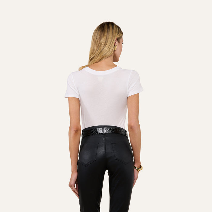 A woman with long blonde hair is seen from behind, wearing the Becca Cotton V-Neck Tee in white, tucked into high-waisted black pants with a black belt, against an off-white background.