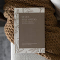 Beside Still Waters Motherhood Book Cover on a brown knitted blanket on the arm of a white couch