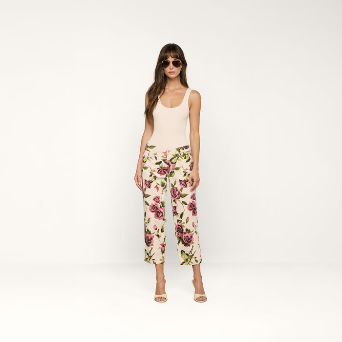 A woman stands facing forward against a plain white background, wearing sunglasses, a beige tank top, and the Blaine Cropped Stovepipe Jean in white with a rose print.