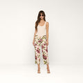 A woman stands facing forward against a plain white background, wearing sunglasses, a beige tank top, and the Blaine Cropped Stovepipe Jean in white with a rose print.