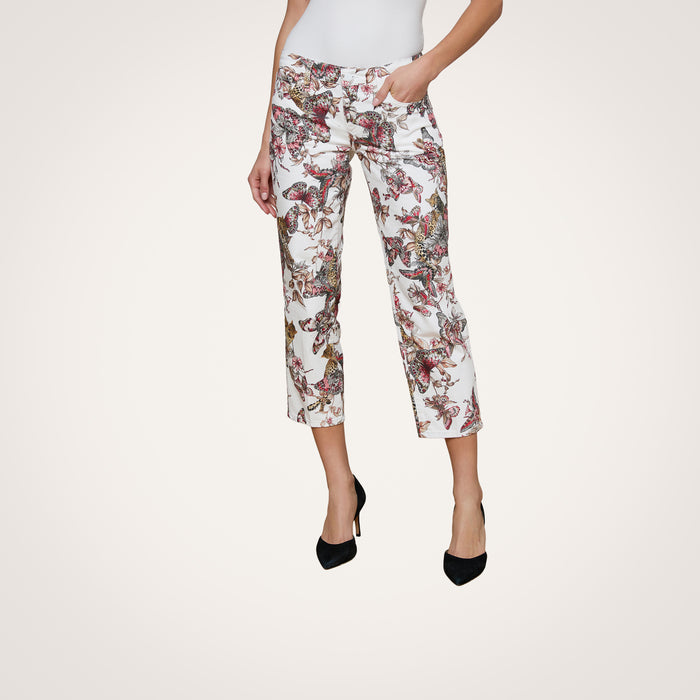 A woman models the Blaine Cropped Stovepipe Jean, featuring a colorful floral and butterfly print on white straight-leg cropped pants. She pairs them with a white top and black high-heeled shoes against a plain light background.