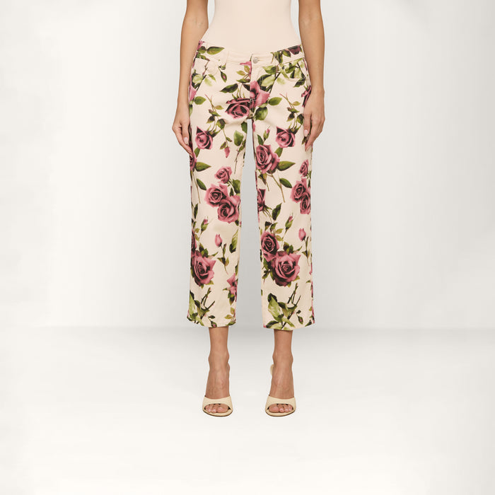 A person wearing the Blaine Cropped Stovepipe Jean in a cream color with a rose print stands against a plain white background, shown from the shoulders down.