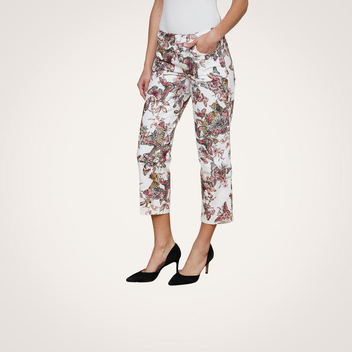 A woman stands against a plain background wearing the Blaine Cropped Stovepipe Jean—white, straight-leg, ankle-length jeans featuring a colorful butterfly print—paired with a white top and black high heels, with one hand in her pocket.