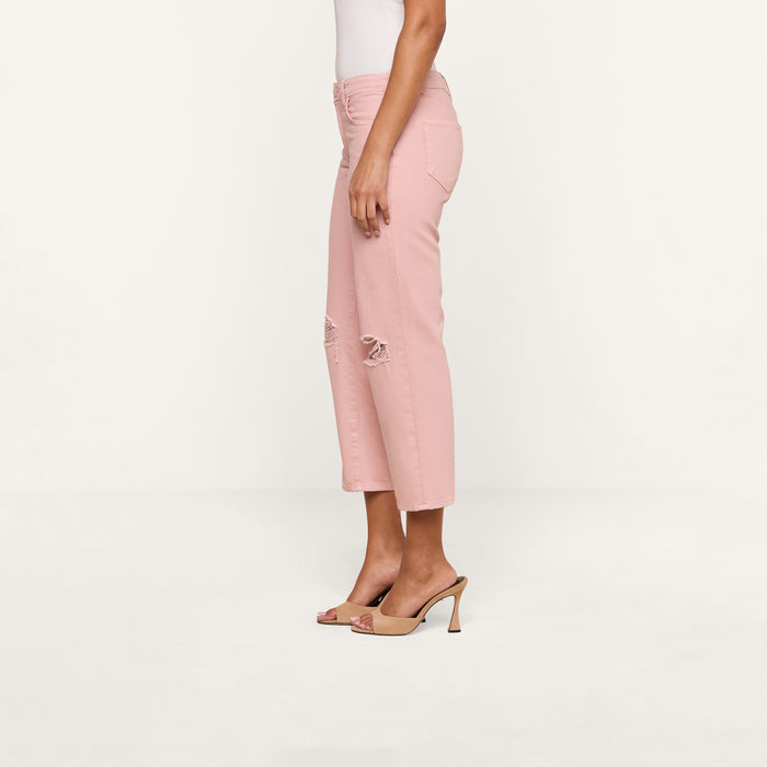 A person wearing the Blaine Cropped Stovepipe Jean in light pink with ripped knees, paired with a white sleeveless top and beige high-heeled sandals, stands sideways against a plain white background.