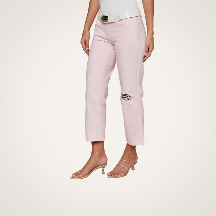 A woman wears the Blaine Cropped Stovepipe Jean in pale pink, styled with a white belt, white tank top, and strappy nude heels. The jeans have a single ripped detail on one knee. The background is plain and off-white.