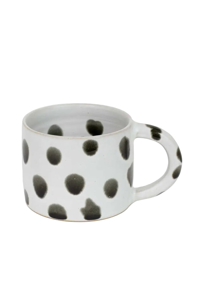 A matte light grey coffee cup with glossy black spots and black dotted pattern on the inside.