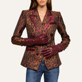 A woman wearing blue jeans, a leopard print blazer with burgundy trim, and the luxurious Boheme Gloves crafted from lambskin leather stands against a plain light background.