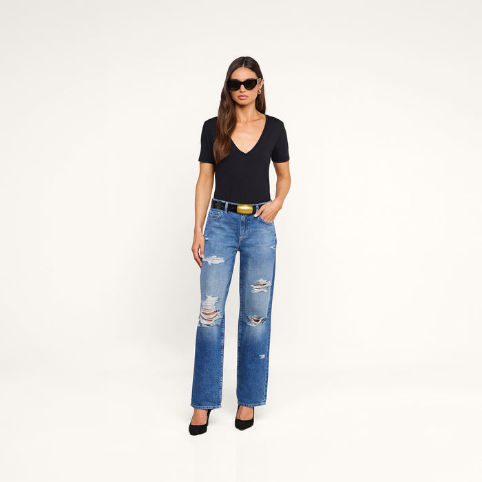 A woman wears the Brianna Cotton V-Neck Tee paired with ripped blue jeans, a black belt, black high heels, and sunglasses as she stands against a plain white background.