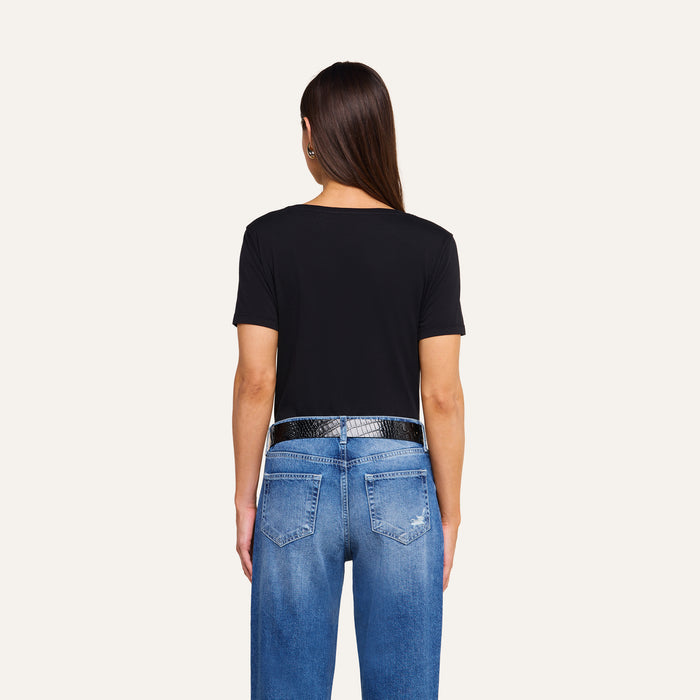 A person with straight brown hair is seen from behind against a plain white background, wearing blue jeans, a shiny black belt, and the Brianna Cotton V-Neck Tee in black, made from Supima cotton.