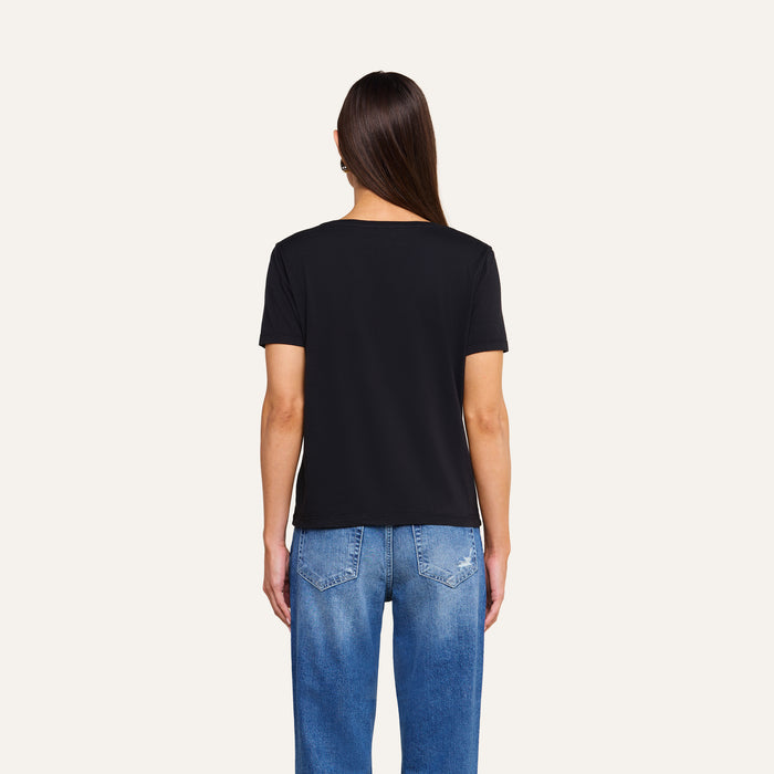 A person with long brown hair, wearing the Brianna Cotton V-Neck Tee in black and blue jeans, is standing with their back to the camera against a plain light background.