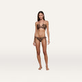 A woman stands on a plain white background wearing the Britt Tie-Side Bikini Bottom in a resort swimwear leopard print, paired with a matching halter neck top.