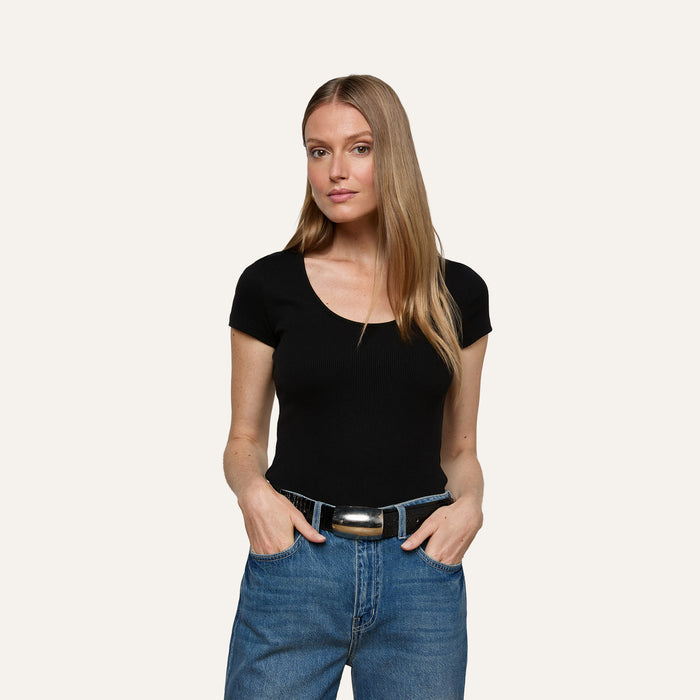 A woman with long, straight blonde hair wears the Brynlee Scoopneck Tee in black and blue jeans, standing with her hands in her pockets against a plain light background.