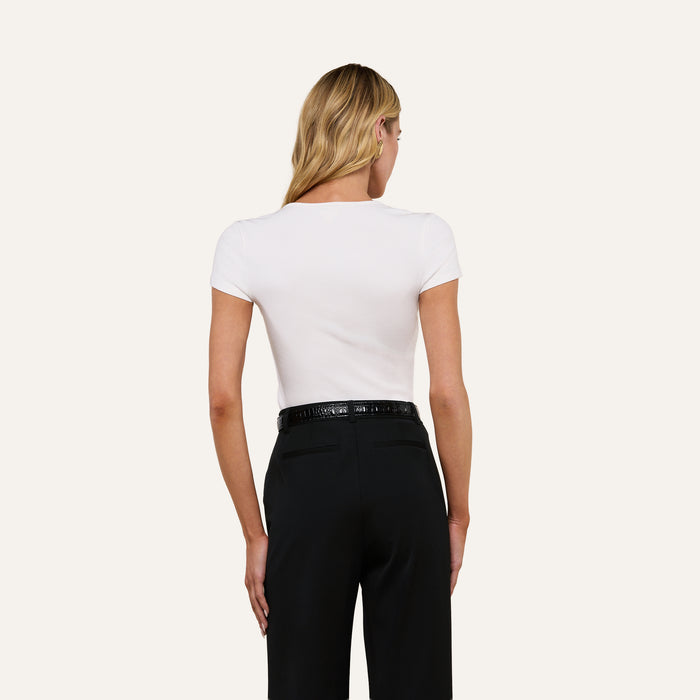 A woman with long blonde hair is shown from the back, wearing the fitted Brynlee Scoopneck Tee in white with short sleeves and high-waisted black pants with a belt.