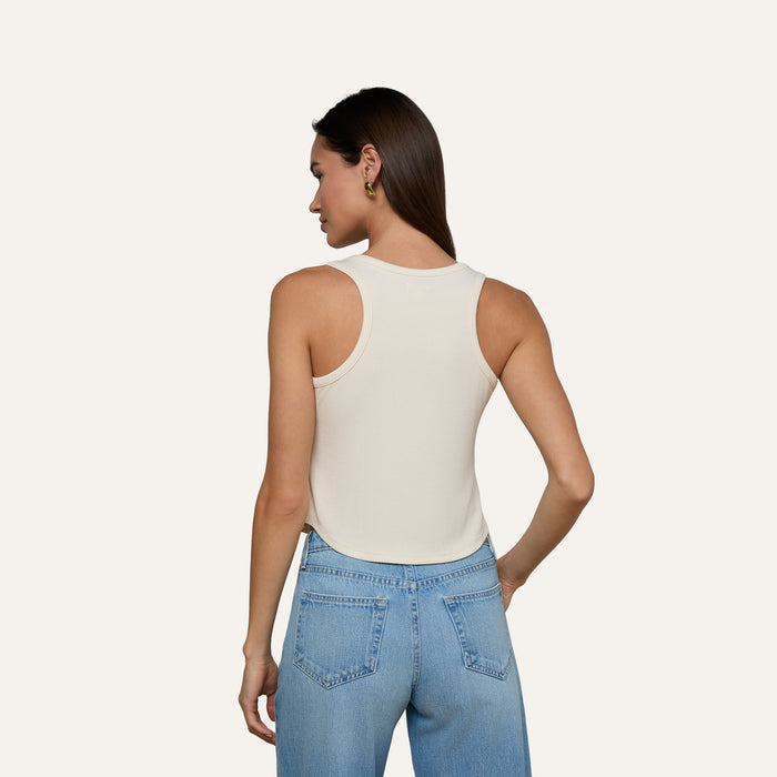 A woman stands with her back to the camera, wearing the Cael Tank Top in white and light blue jeans, set against a plain light background.
