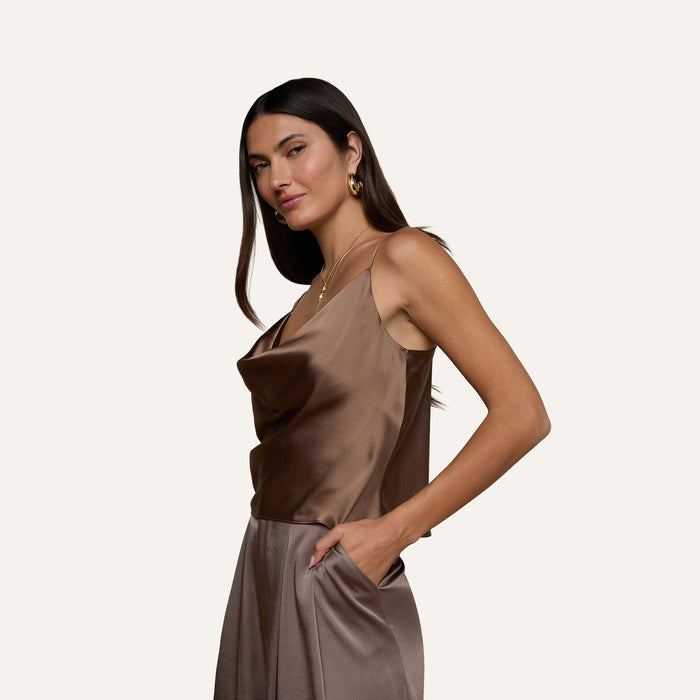 A woman wearing the Calista Silk Camisole and matching high-waisted pants stands with one hand in her pocket, looking confidently at the camera against a plain light background.