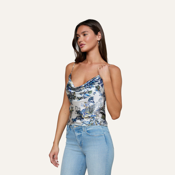 A woman wearing light blue jeans and the Calista Silk Camisole, featuring a blue butterfly print, stands against a plain, light background.