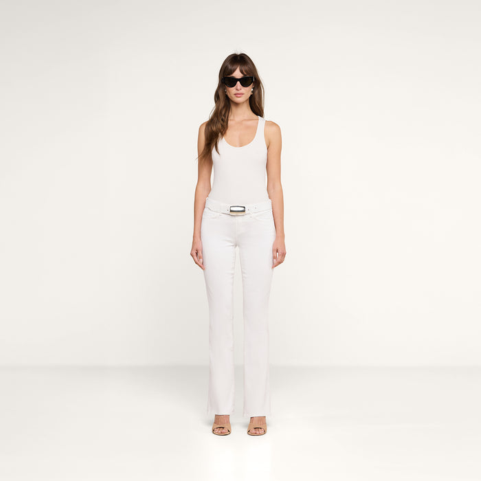 A woman wearing sunglasses, a white sleeveless top, the Cara Low-Rise Bootcut Jean with a belt, and heels stands facing forward against a plain white background.