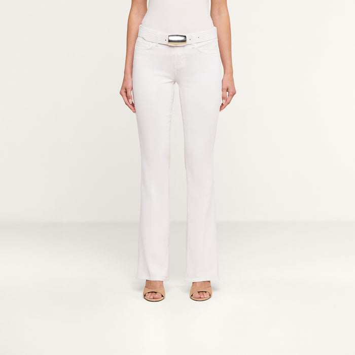 A person wearing the Cara Low-Rise Bootcut Jean in white, paired with a matching white top, a white belt with a rectangular buckle, and beige open-toe heels stands against a plain white background.