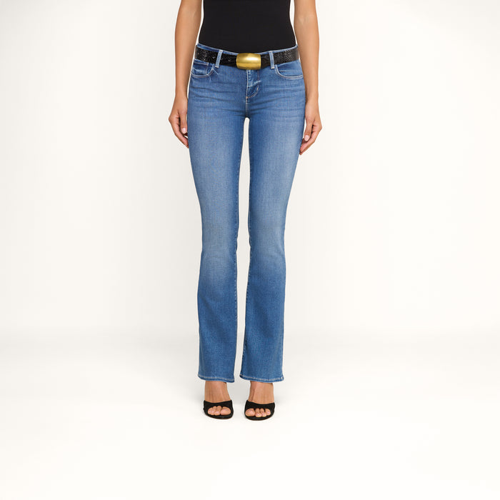 A person wears the Cara Low-Rise Bootcut Jean in blue stretch denim with a black sleeveless top, black belt featuring a gold buckle, and black open-toe heels, standing against a plain white background. Only their lower body is visible.