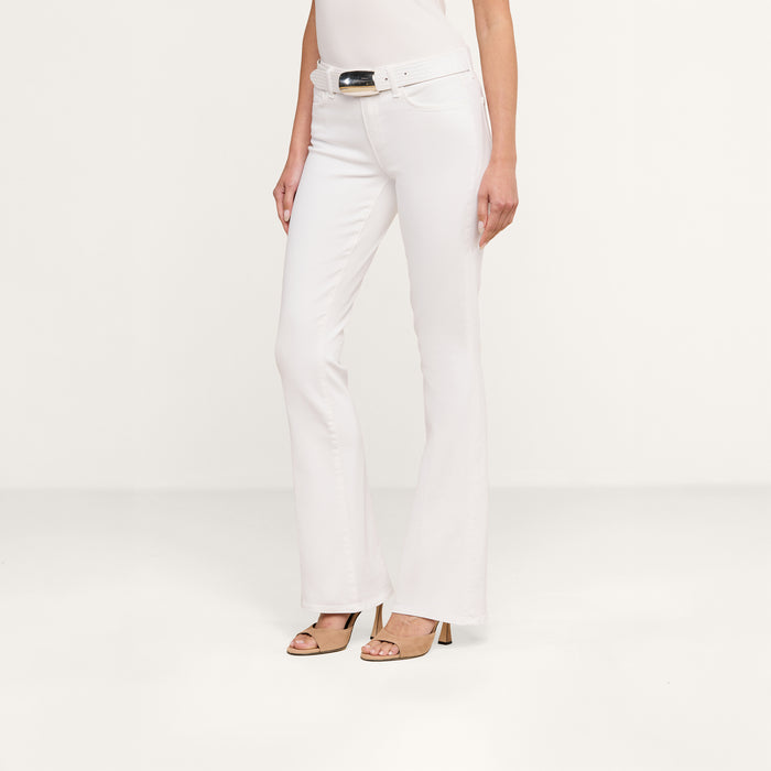 A woman wearing the Cara Low-Rise Bootcut Jean in white, styled with a white belt featuring a large buckle and tan heeled sandals, stands against a plain white background.