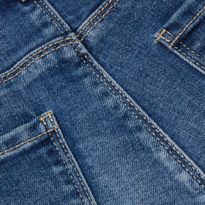 Close-up of the Cara Low-Rise Bootcut Jean in stretch denim blue, highlighting the back pockets, seams, and distinctive orange stitching. The texture and weave of the fabric are clearly visible.