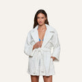 A woman wearing the Caterina Cover-Up Robe, a white textured cotton kimono style, over a blue top stands against a plain light background, looking at the camera.