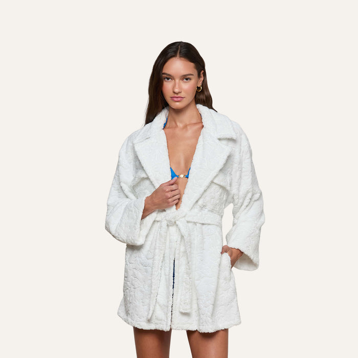 A woman wearing the Caterina Cover-Up Robe, a white textured cotton kimono style, over a blue top stands against a plain light background, looking at the camera.