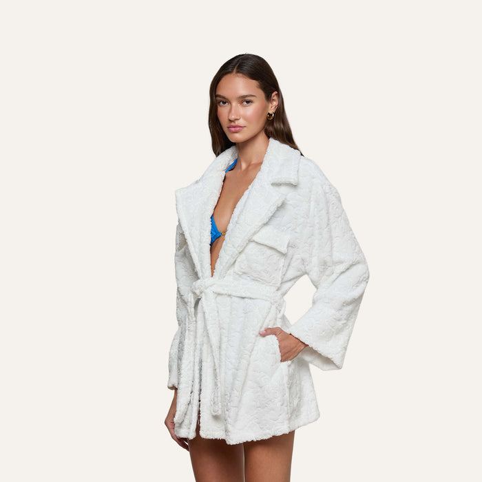 A woman wears the Caterina Cover-Up Robe, a short, white, quilted kimono-style robe with a belt, layered over a blue bikini as she stands against a plain light background.