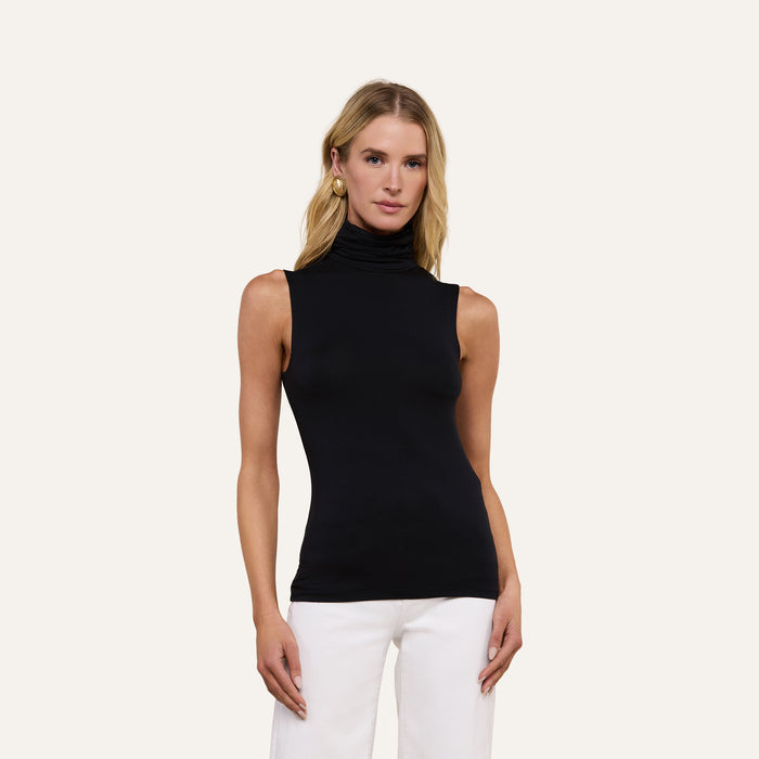 A woman wearing the Ceci Sleeveless Turtleneck in black and white pants stands against a plain light background, looking at the camera with a neutral expression.
