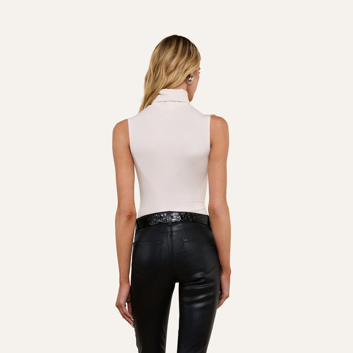 A woman with long blonde hair is shown from behind against a plain light background, wearing the Ceci Sleeveless Turtleneck in white and slim fit black leather pants.