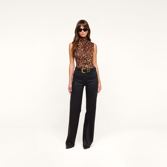 A woman wearing sunglasses, the Ceci Sleeveless Turtleneck in a leopard print, and slim fit high-waisted black pants stands against a plain white background.
