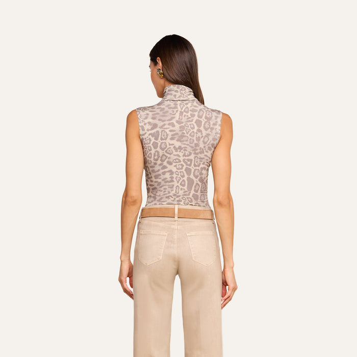 A woman faces away from the camera, wearing the Ceci Sleeveless Turtleneck in a grey leopard print paired with beige pants featuring visible back pockets, set against a plain light background.
