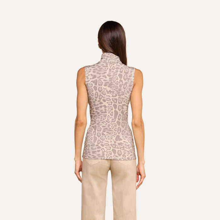 A woman stands with her back to the camera, wearing the Ceci Sleeveless Turtleneck in a light brown animal print and beige pants, set against a plain light background.